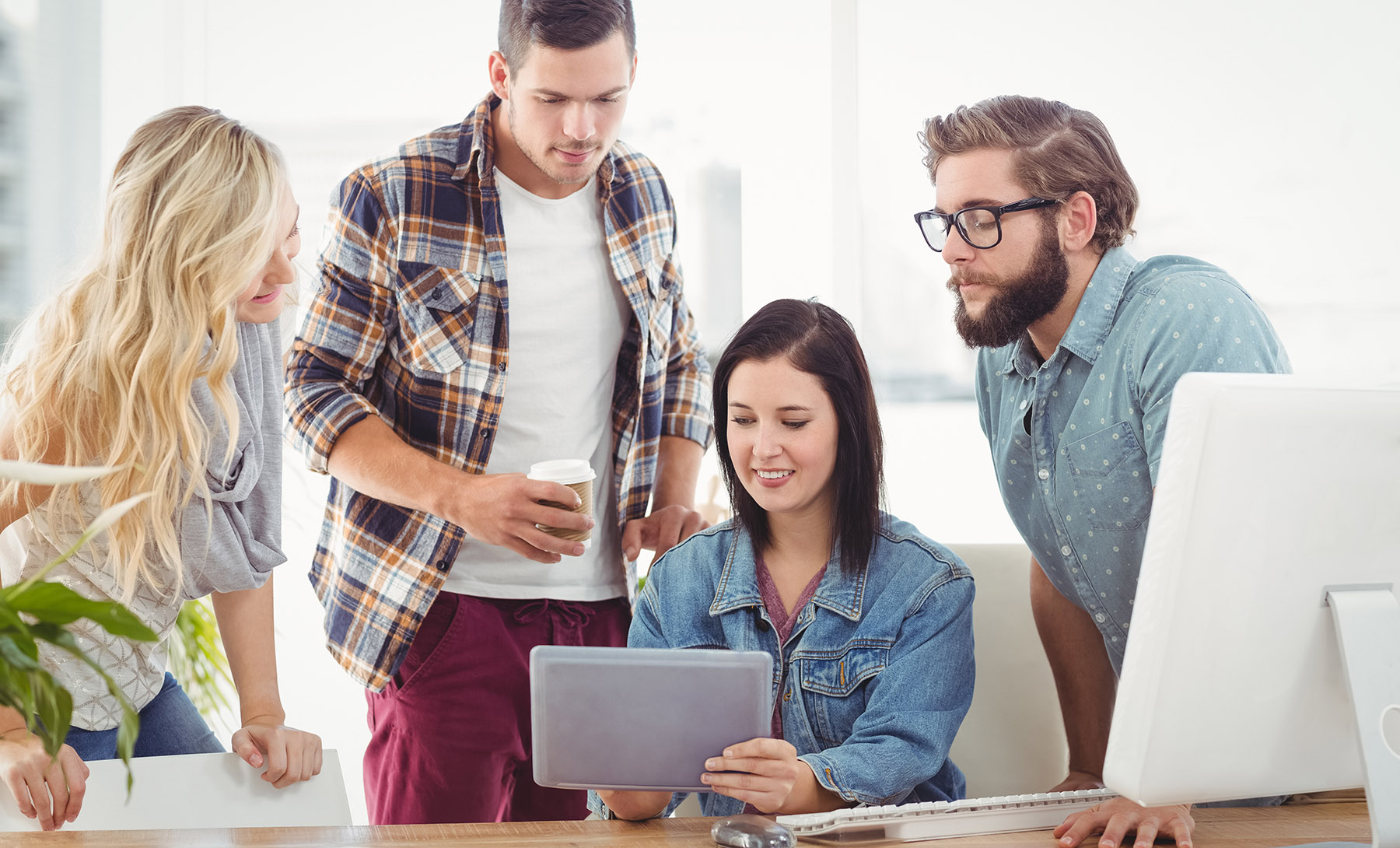 Vier junge Menschen an einem Tisch, mit Computer und Tablet - Marketing-Manager (m/w/d) bei Kuthan-Immobilien gesucht