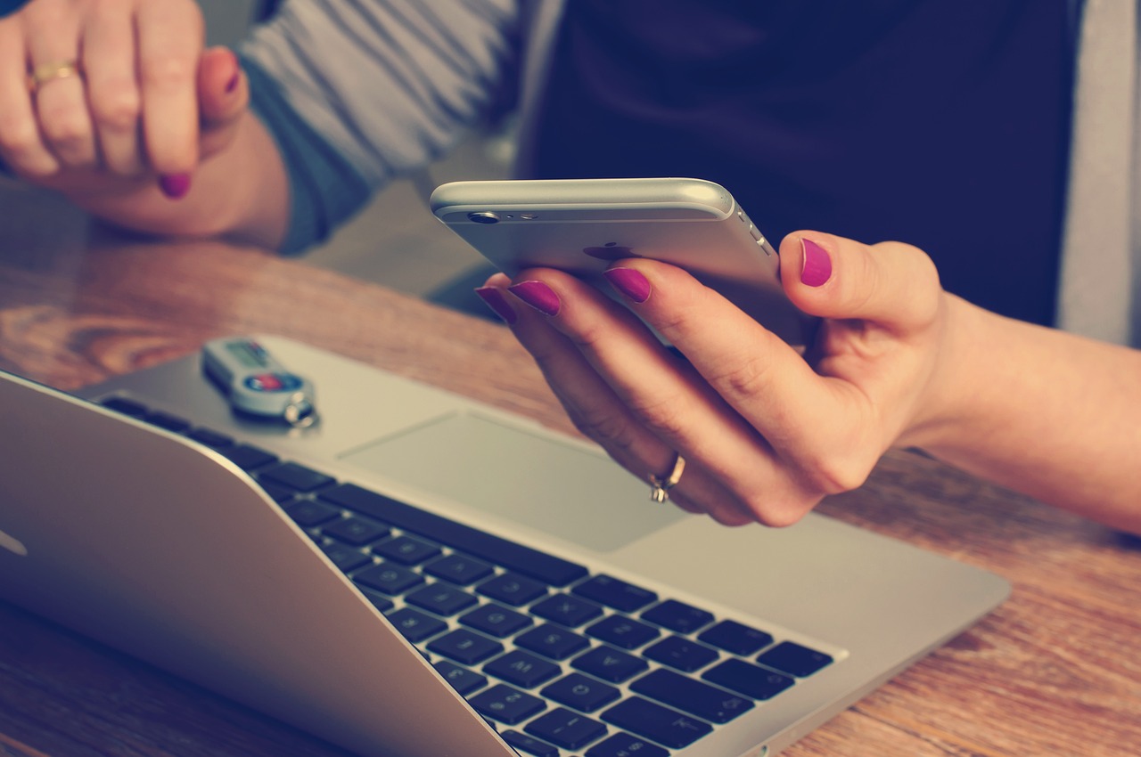 Frau hält Handy in der Hand und sitzt vor Laptop - Bild für Kuthan-Aktuelles